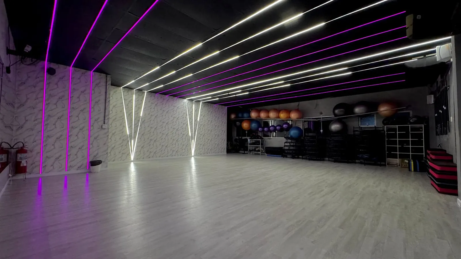 Sala de aulas coletivas da FitCompany São Pedro com iluminação em neon e bolas de ginástica